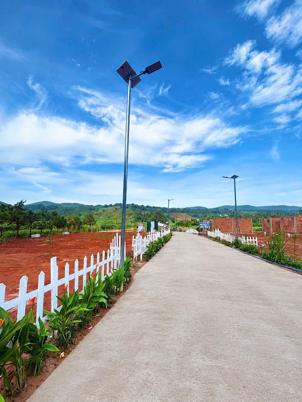 Đường bê tông nội khu cụm 5 lô Mê Linh, Nam Ban: đèn năng lượng mặt trời, hàng rào trắng, đồi xanh phía xa