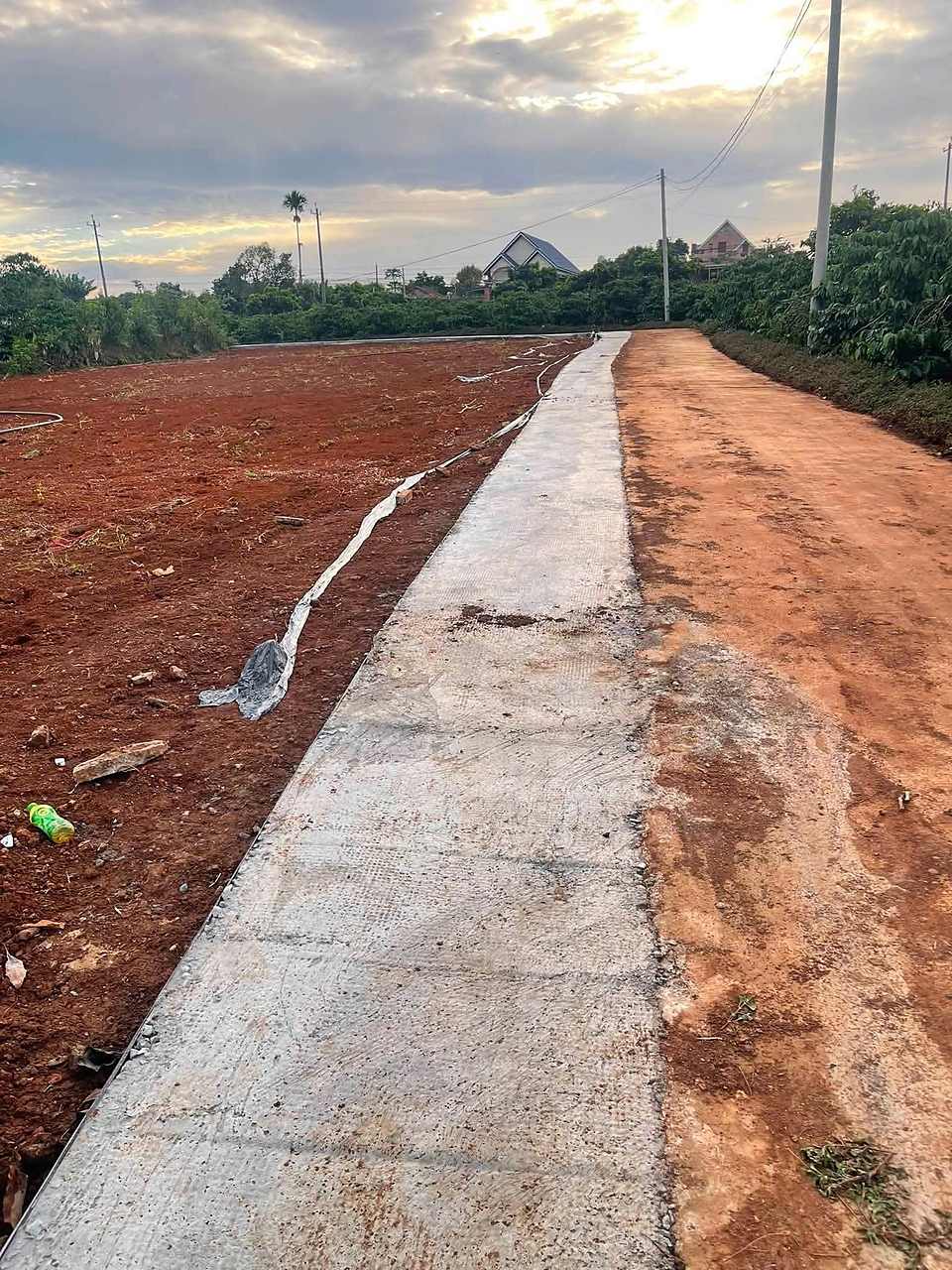 Cụm nền F0 gần hồ Bãi Công Nam Ban – đất đã dọn bằng phẳng, đường bê tông, khu dân cư, hoàng hôn