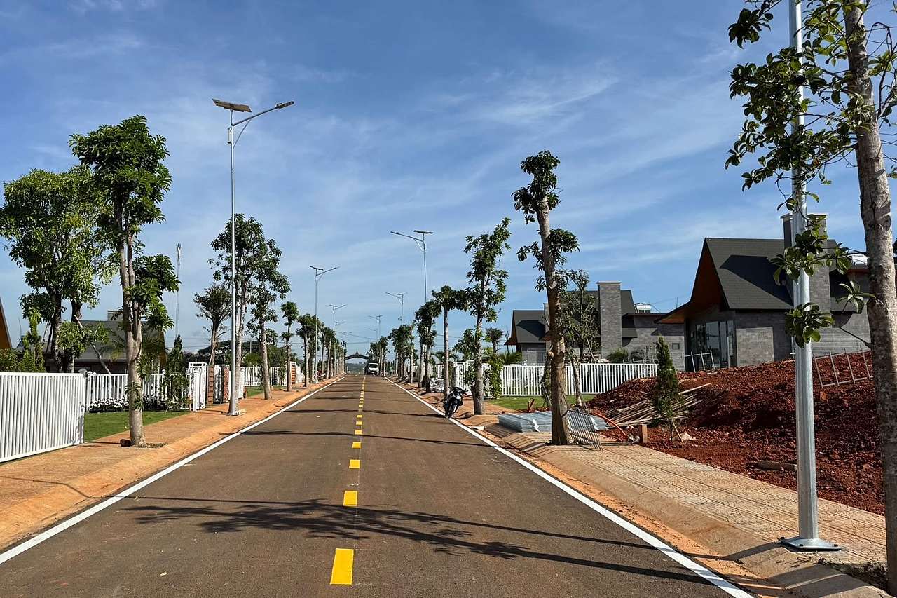 Đường nhựa nội khu Thiên Vân Village có vạch kẻ, đèn năng lượng mặt trời, cây xanh và hàng rào trắng