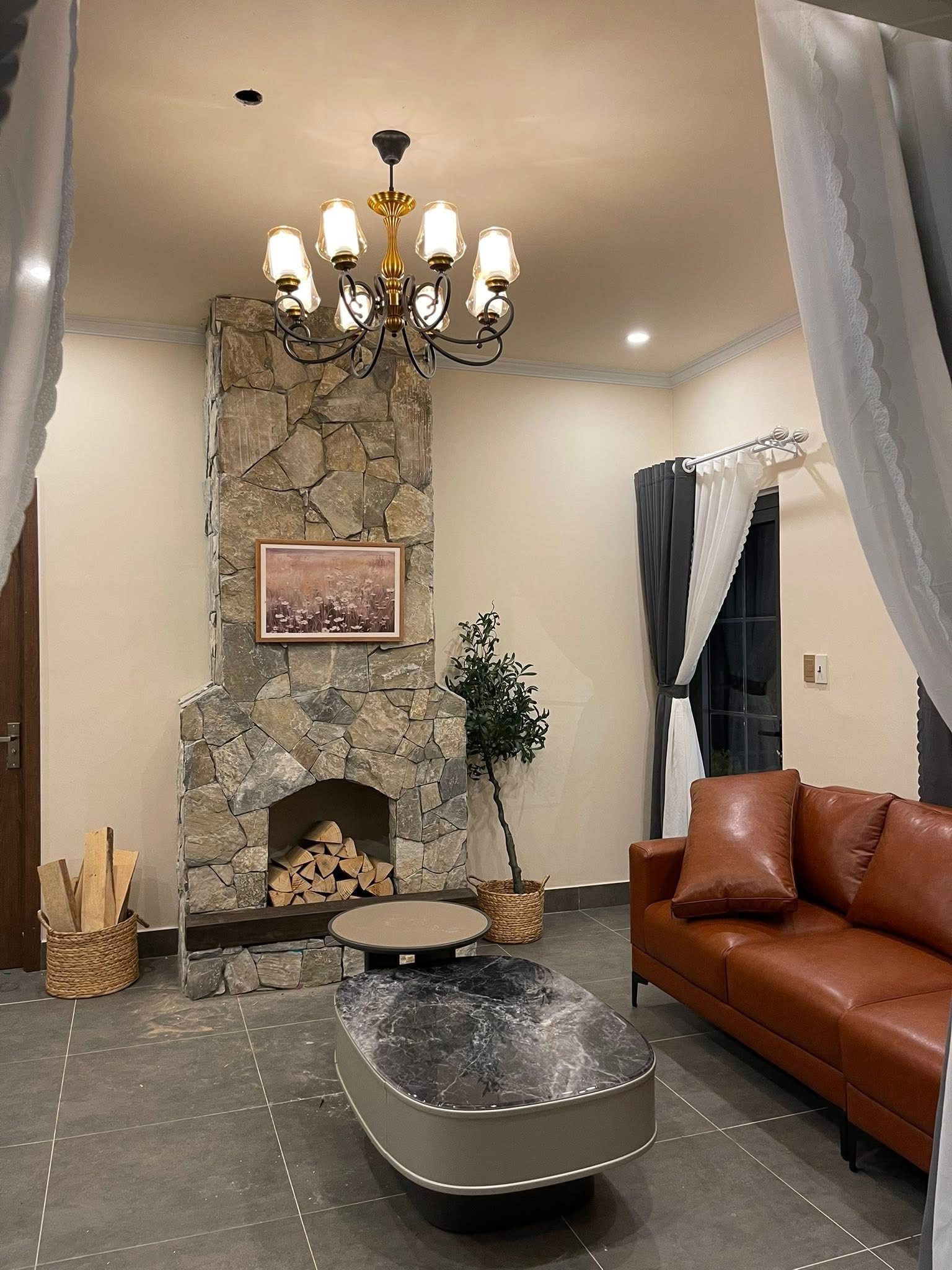 Hill House Retreat Nam Ban – phòng khách lò sưởi đá, sofa da bò, đèn chùm đồng