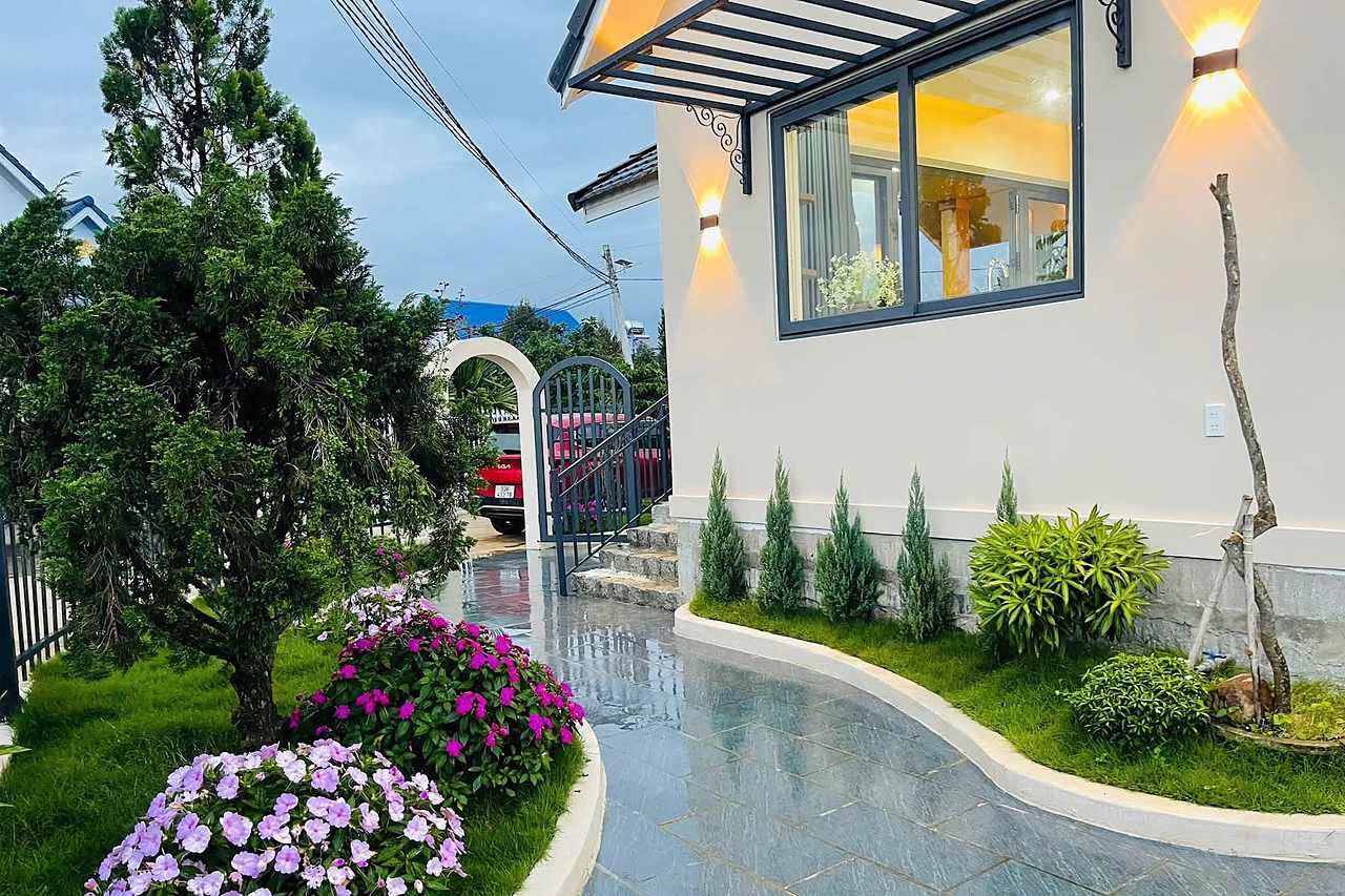 Hill House Village Nam Ban – sân vườn lối đá, hoa, nhà lên đèn lúc hoàng hôn