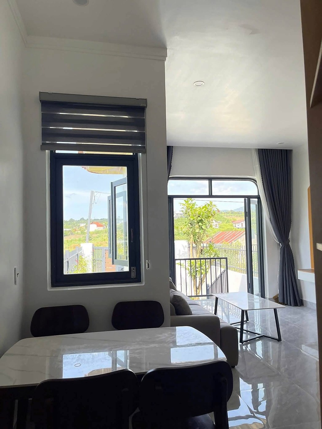 Bàn ăn mặt đá và phòng khách, cửa kính lớn nhìn ra ban công view đồi