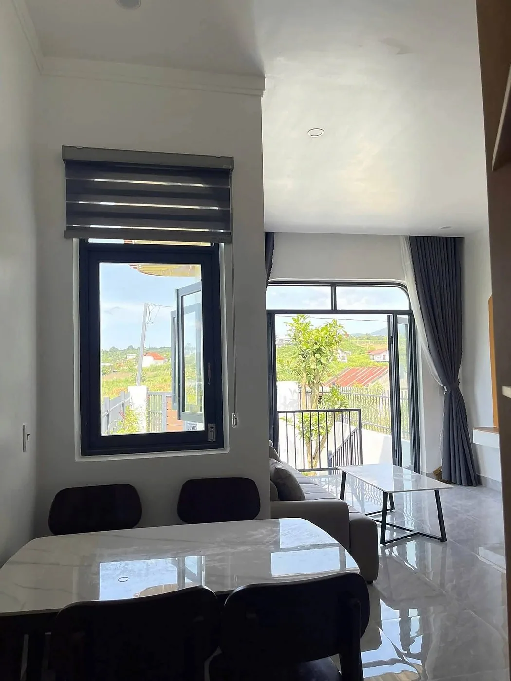 Bàn ăn mặt đá và phòng khách, cửa kính lớn nhìn ra ban công view đồi