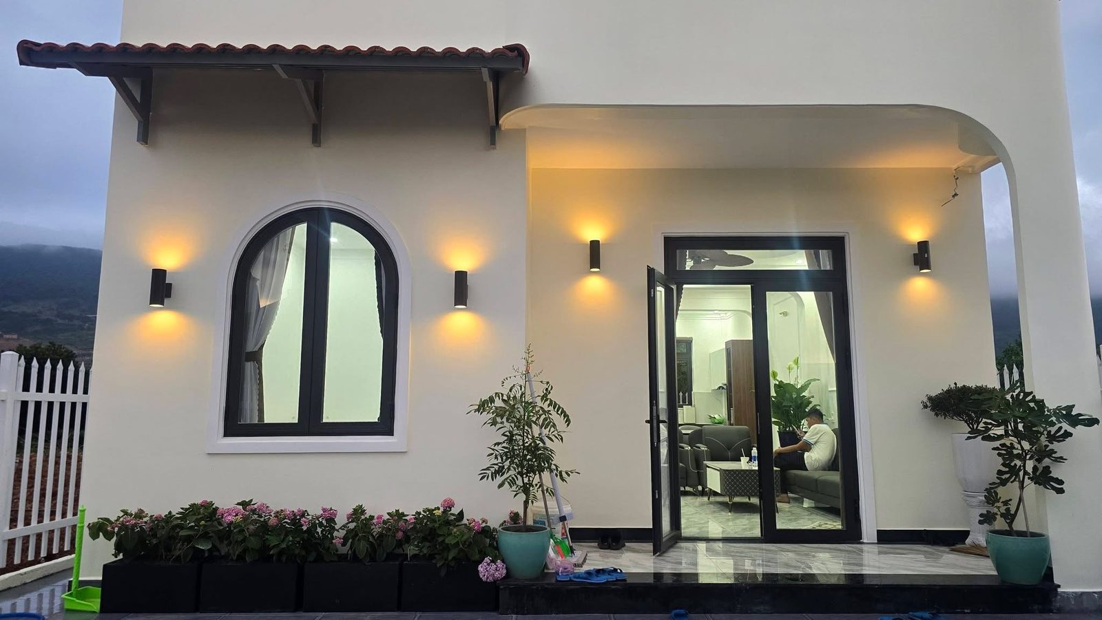 Hiên nhà và cửa kính vào phòng khách, đèn tường ấm, sân hoa cẩm tú cầu