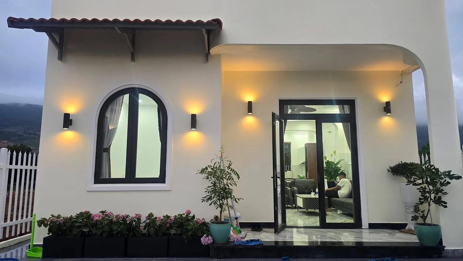 Hiên nhà và cửa kính vào phòng khách, đèn tường ấm, sân hoa cẩm tú cầu