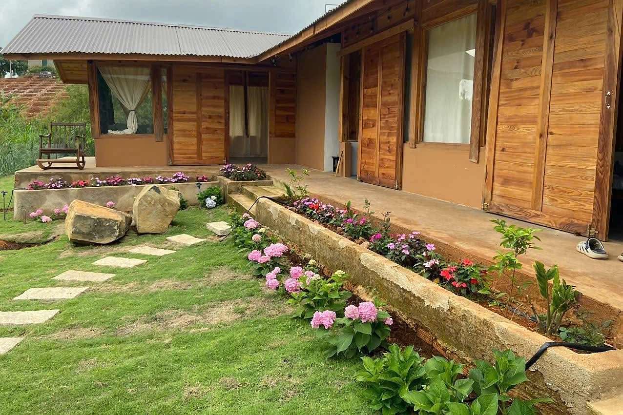 Mặt trước nhà gỗ Nam Ban – bồn hoa cẩm tú cầu, hiên gỗ, sân cỏ xanh và lối đá
