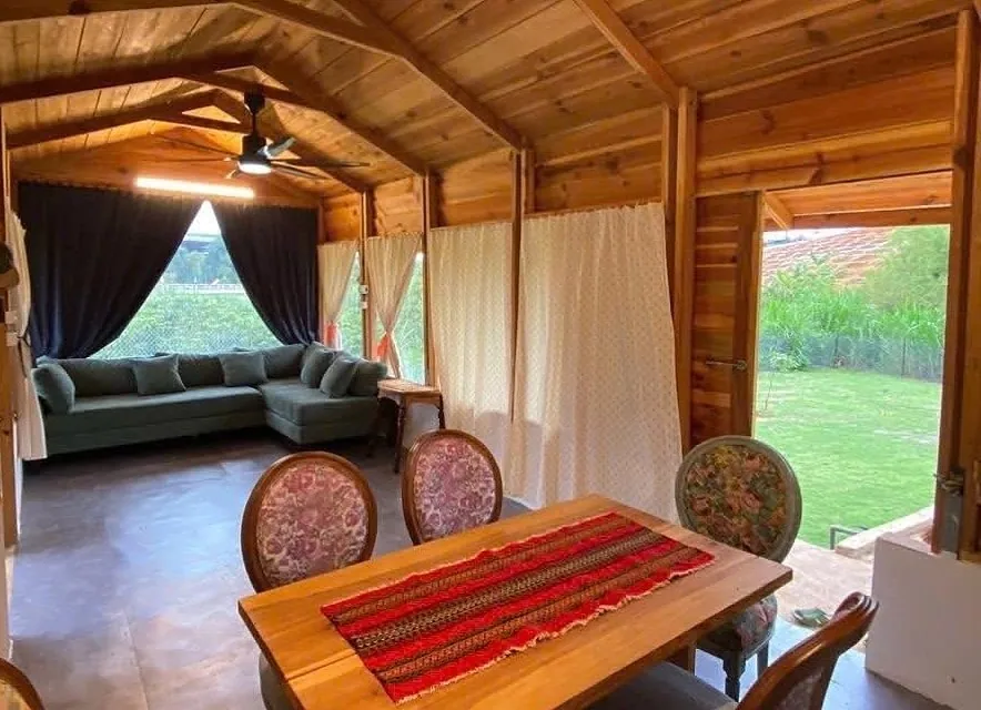 Bên trong nhà gỗ – trần gỗ vòm, bàn ăn gỗ, bộ sofa nhìn ra sân vườn