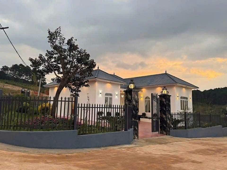 Biệt thự lô góc Nam Ban lúc hoàng hôn – nhà mái Thái trắng, cổng đá, sân vườn đèn vàng, giữa rừng thông