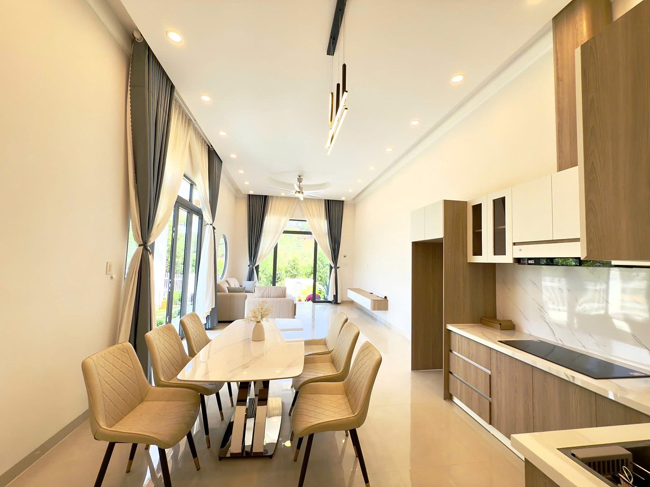 Khu bếp và bàn ăn 6 ghế — bếp gỗ mặt đá, bếp từ, cửa kính lớn ra sân, view đồi
