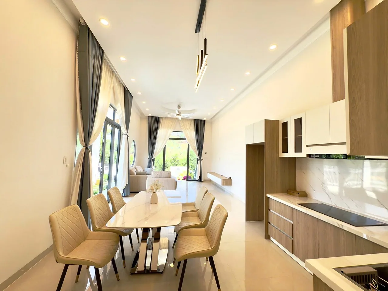 Khu bếp và bàn ăn 6 ghế — bếp gỗ mặt đá, bếp từ, cửa kính lớn ra sân, view đồi