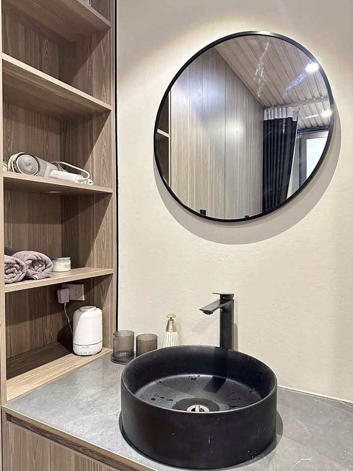 Khu lavabo nhà nghỉ dưỡng Mê Linh, Nam Ban: chậu đá đen, gương tròn, tủ kệ gỗ