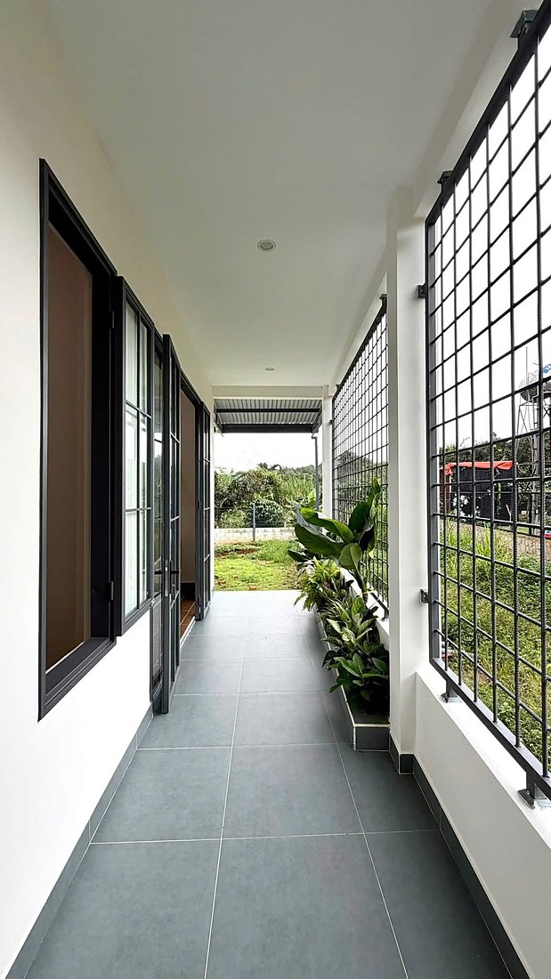 Hành lang bên hông nhà nhìn ra sân vườn, bồn cây xanh, cửa kính khung sắt
