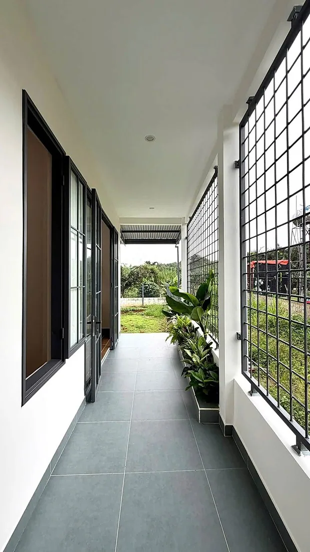 Hành lang bên hông nhà nhìn ra sân vườn, bồn cây xanh, cửa kính khung sắt