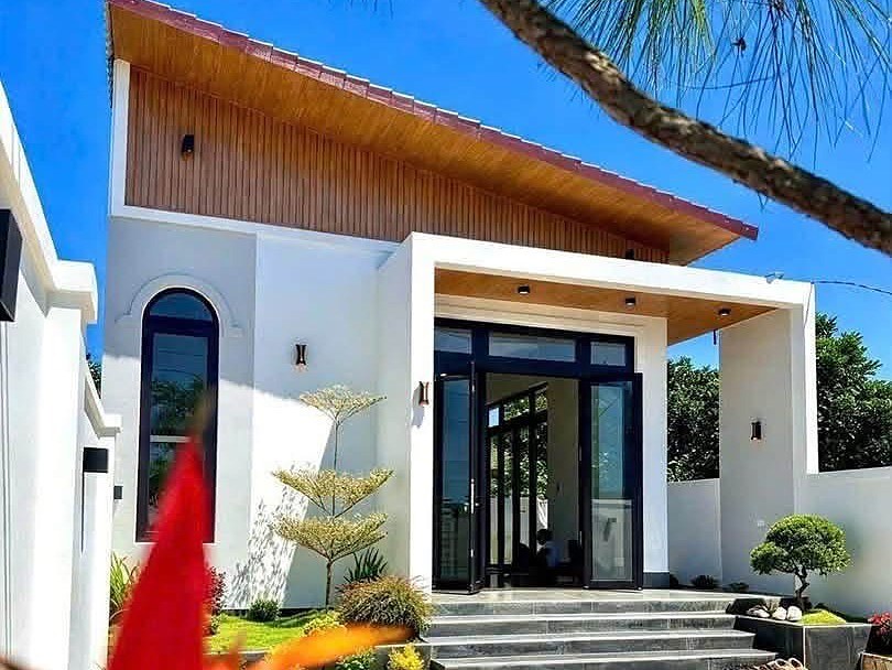 Nhà sân vườn mới ở Nam Ban: nhà trệt tường trắng, mái ốp gỗ, cửa kính lớn, bậc thềm đá, sân lát gạch đá