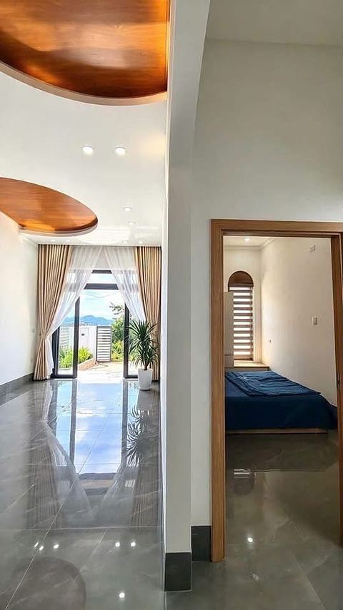 Phòng khách trần gỗ cong, sàn gạch bóng, cửa kính mở ra sân nhìn về đồi; cửa phòng ngủ bên phải