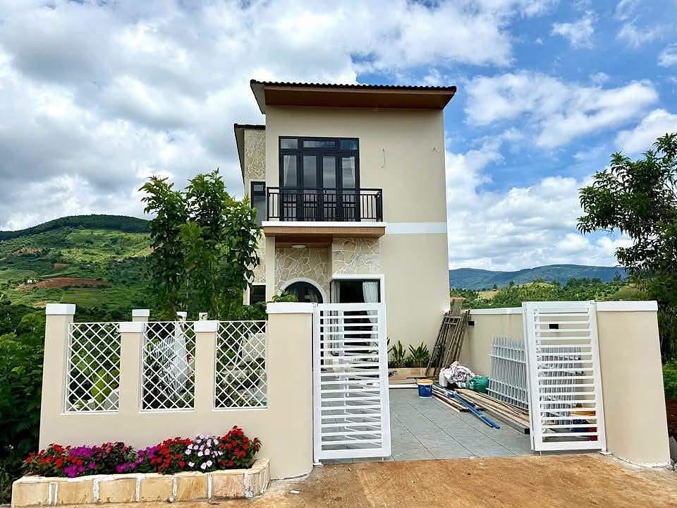 Mặt tiền nhà vườn mới 2 tầng Nam Ban – tường kem ốp đá, ban công, cổng trắng, bồn hoa, view đồi