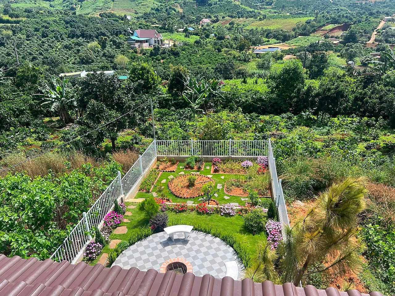 Sân vườn phía sau nhìn từ tầng trên: lối đá, bồn hoa, khu BBQ tròn, vườn cà phê và thung lũng phía xa