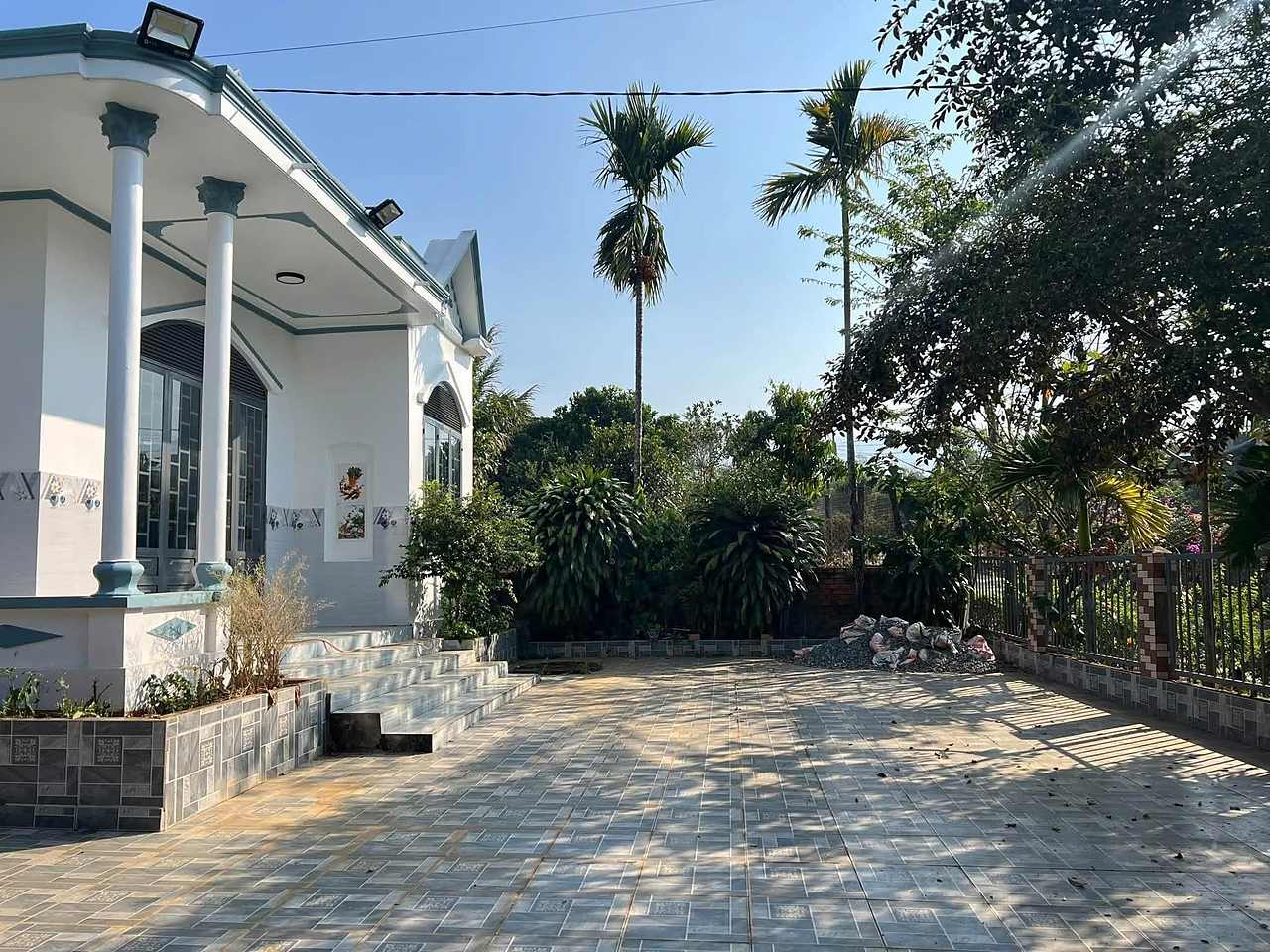 Góc nhà và sân lát gạch, hàng cau và vườn cây