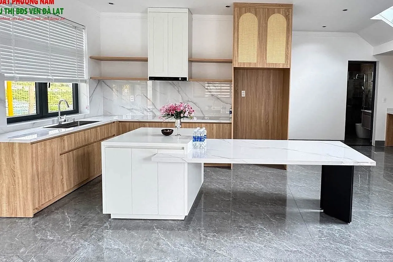 Bếp hiện đại bàn đảo đá marble, tủ bếp gỗ, cầu thang kính lên gác