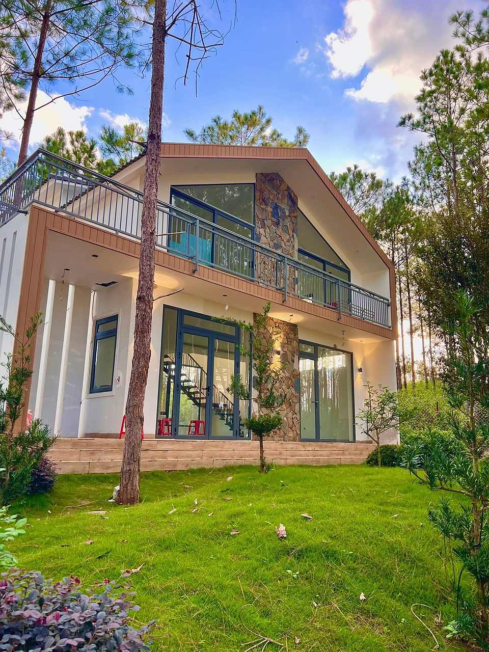 Mặt trước villa đá ốp 1 trệt 1 lầu HT86 Nam Ban, gable kính lớn, sân cỏ giữa rừng thông