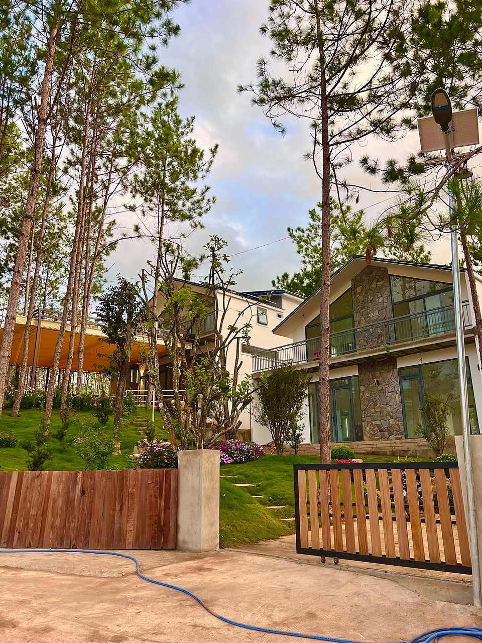 Cổng gỗ và sân villa HT86 Nam Ban, vườn hoa bậc thang, mái hiên bạt và rừng thông