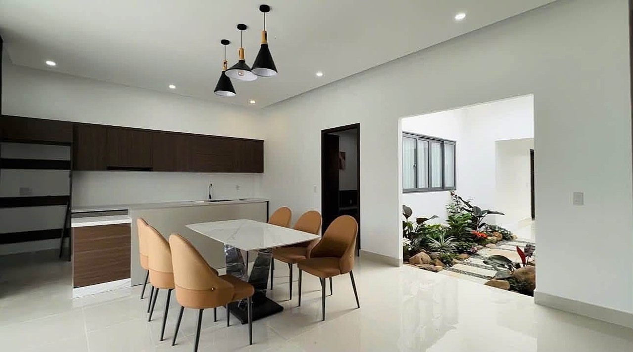 Bếp và bàn ăn villa Nam Ban mở ra giếng trời cây xanh, đèn thả, tủ bếp gỗ