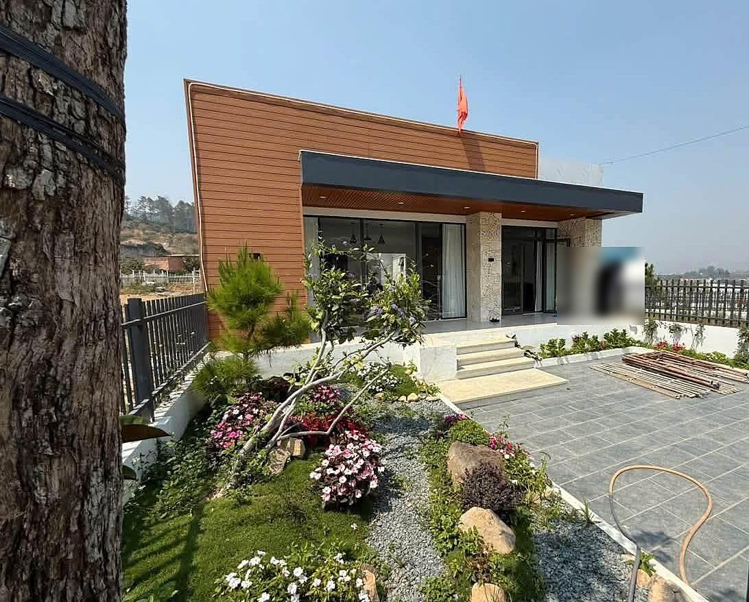 Mặt tiền villa nghỉ dưỡng Nam Ban ốp gỗ và đá, hiên kính lớn, sân lát đá và vườn hoa